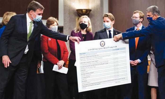 Sen. Joe Manchin (R), Democrat of West Virginia, hands a poster describing a proposal for a Covid relief bill to Sen. Mark Warner (L), Democrat of Virginia, alongside a bipartisan group of Democrat and Republican members of Congress as they announce the proposal on Capitol Hill, on December 1, 2020. (Photo/SAUL LOEB/AFP via Getty Images)