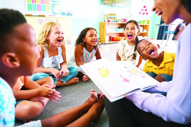 school teacher reads a story to a multi-cultural class seated in the classroom. stock photo