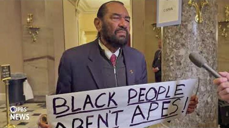 Representative Al Green holds a sign that reads, “Black People Aren’t Apes.” (Photo PBS)