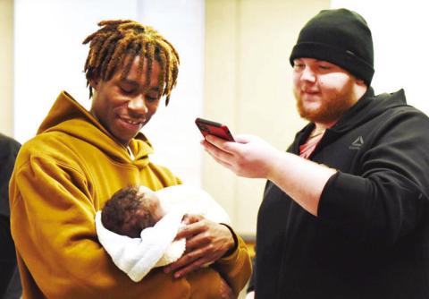 Carter, 19, holds his newborn son, Tymere, as another soon-to-be father takes their photo on Thursday, Dec. 19, 2024, as part of a program called Dad Prep Academy at DeLaSalle High School in Kansas City (Anna Spoerre/Missouri Independent).