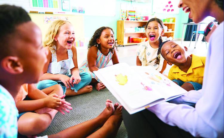 school teacher reads a story to a multi-cultural class seated in the classroom. stock photo