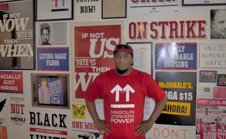 Terrence Wise stands in front of a wall of campaign posters at Missouri Workers Power’s Kansas City headquarters. (Thomas White/The Beacon)