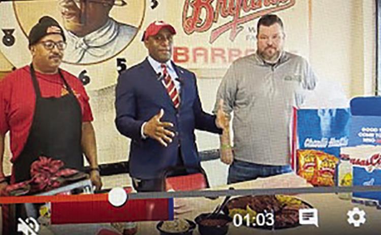 KCMO Mayor Quinton Lucas (center) at Arthur Bryant’s Barbecue today (Thursday) showing an array of items he has wagered with Cincinnati Mayor Aftab Pureval. photo/screenshot
