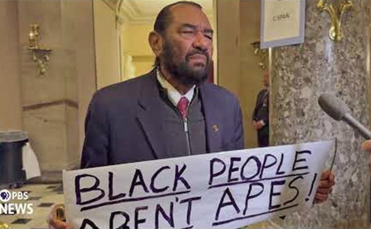 Representative Al Green holds a sign that reads, “Black People Aren’t Apes.” (Photo PBS)
