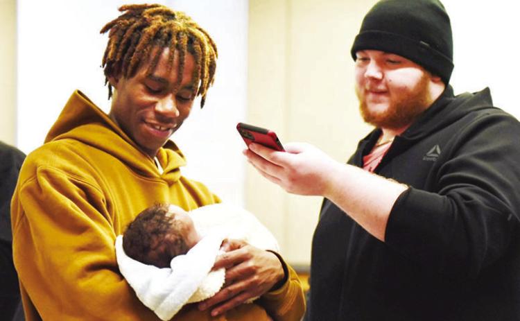 Carter, 19, holds his newborn son, Tymere, as another soon-to-be father takes their photo on Thursday, Dec. 19, 2024, as part of a program called Dad Prep Academy at DeLaSalle High School in Kansas City (Anna Spoerre/Missouri Independent).